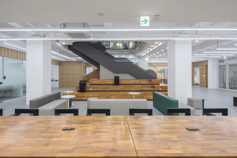 Central staircase with timber treads and black steel stringers flanked by white columns and modular seating
