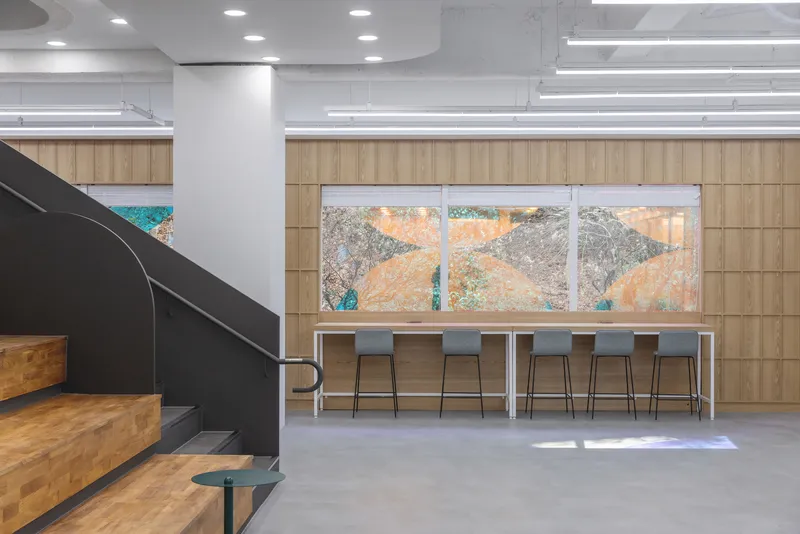 High counter with timber stools facing a vertical-grain wood wall and large window in afternoon light