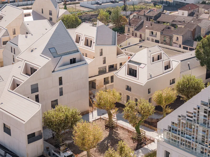 Aerial view of clustered pale concrete housing volumes around a central courtyard with young deciduous trees