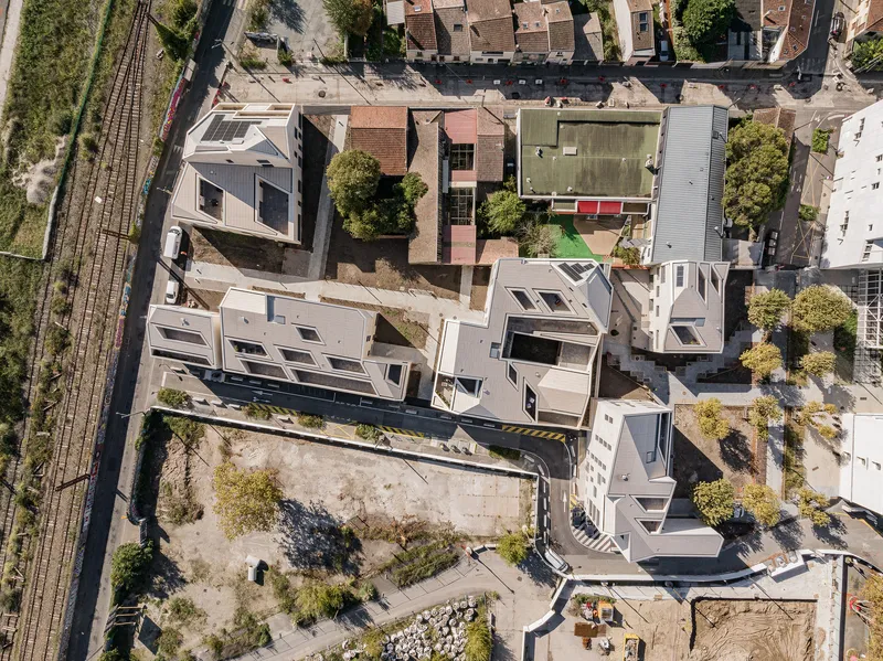Drone view of angled residential blocks with varied rooflines alongside railway tracks and neighboring rooftops