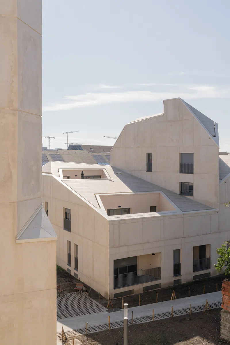 Pale concrete facade with staggered roofline and punched window openings under an overcast sky