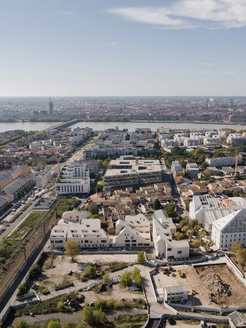 Aerial overview of the low-rise housing complex among railway lines with a river and distant skyline