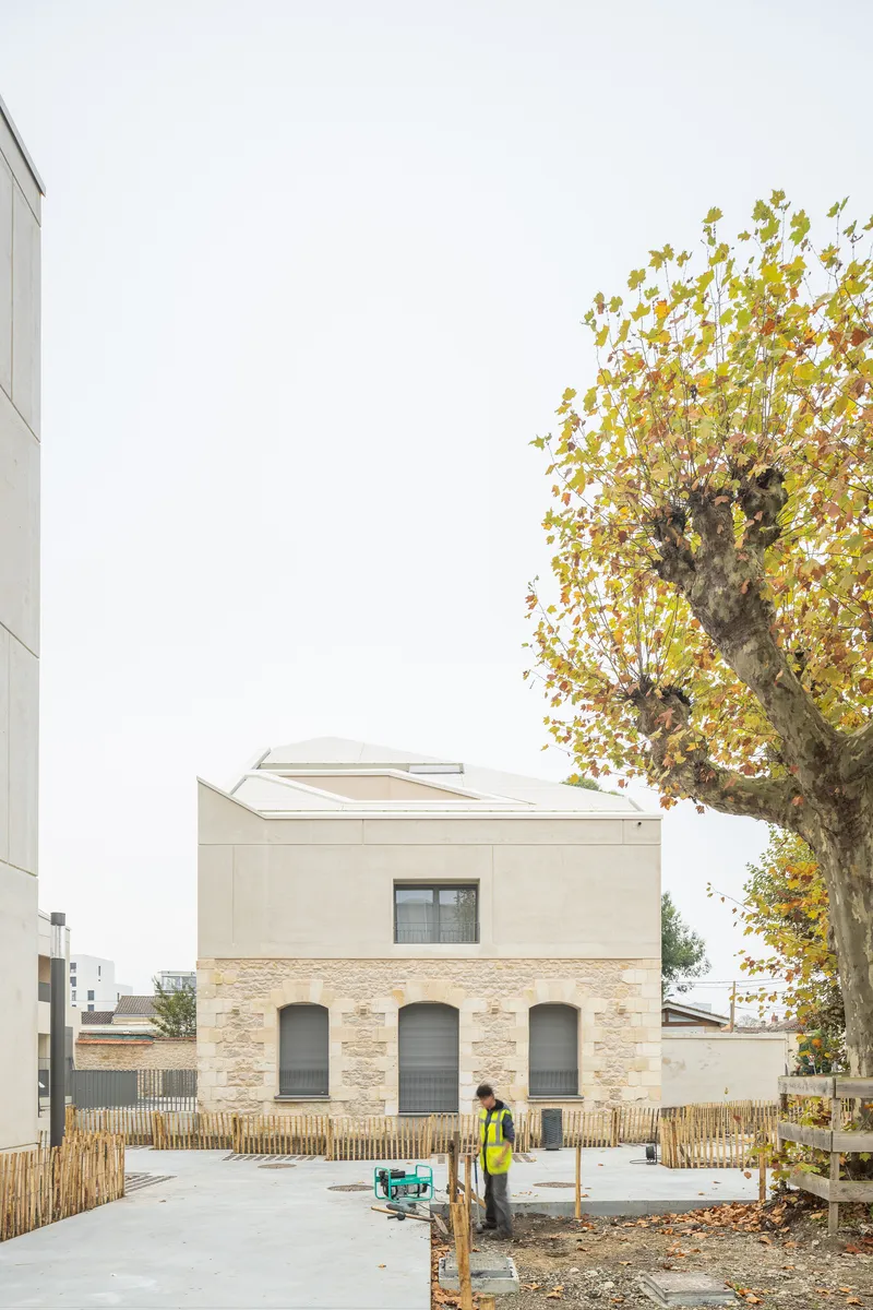 Street view of the stone base and rendered upper floor with a worker and autumn tree in front