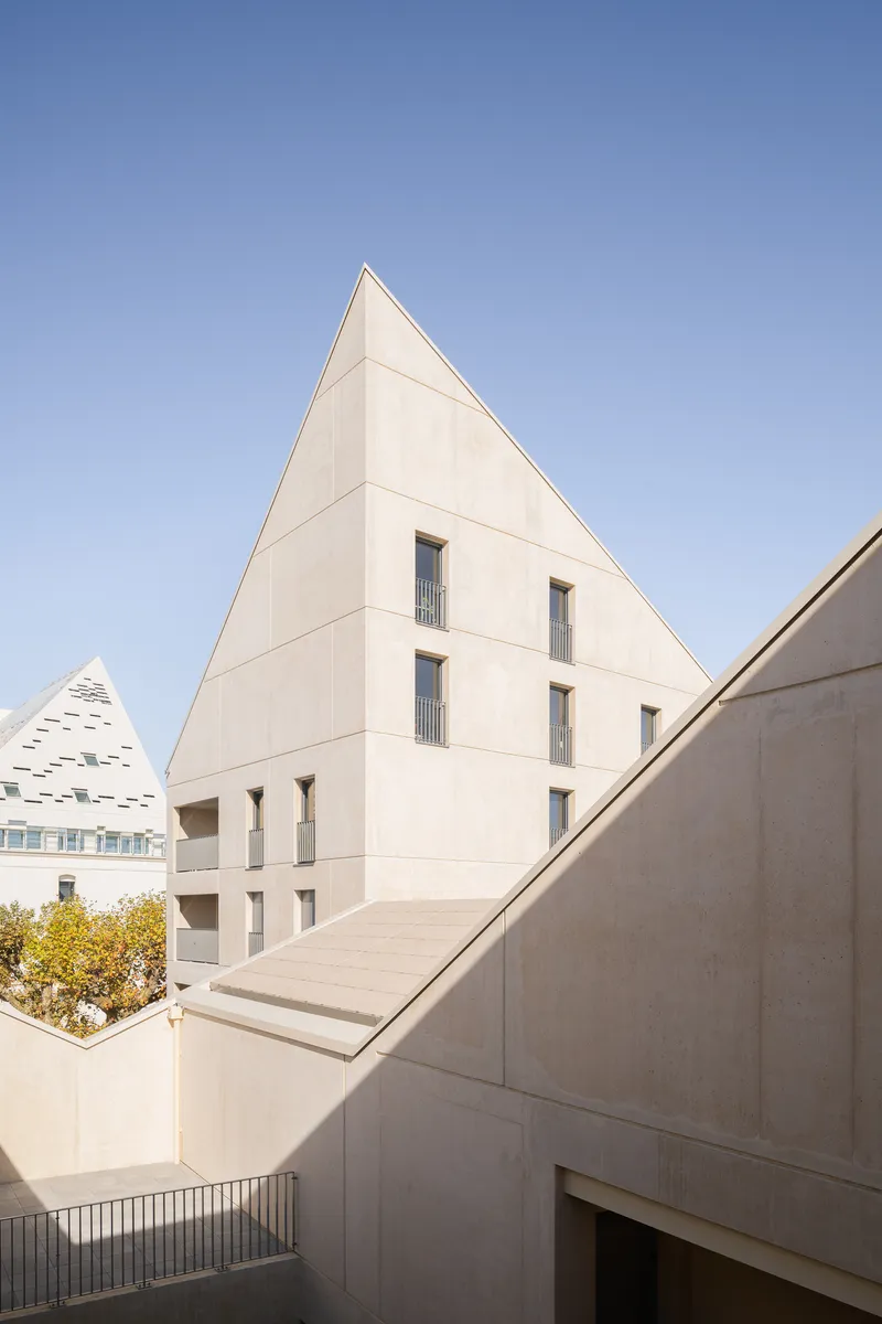 Triangular gable facade with tall windows rising above the courtyard under a clear blue sky