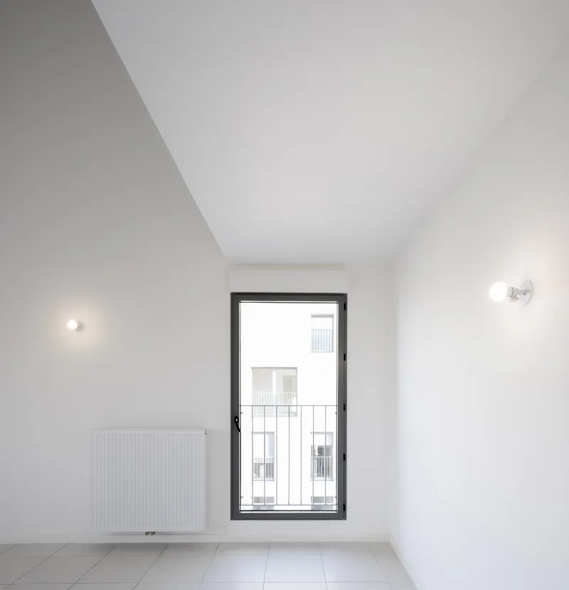 White interior room with a tall narrow window, wall-mounted sconces, and a panel radiator