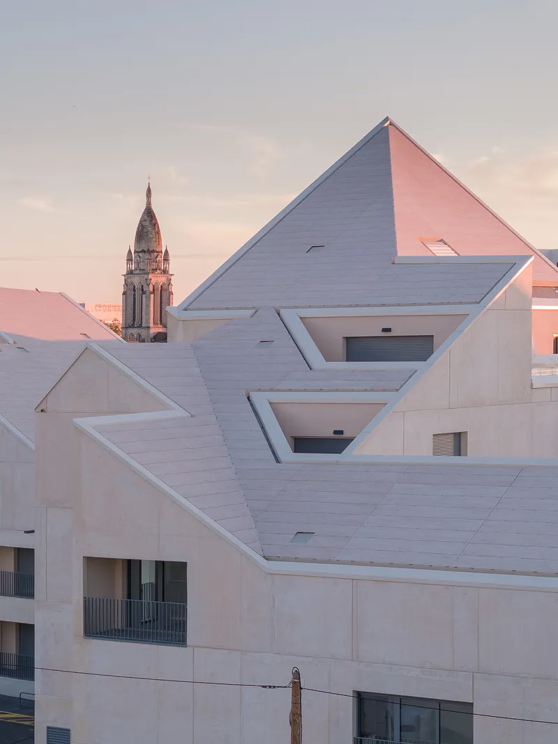 Stepped roofline with triangular gables and recessed balconies at dusk with a church tower beyond