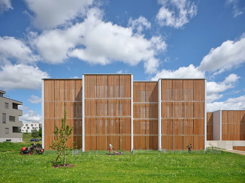 Vertical timber slatted facade with white horizontal frames viewed across a grass lawn with children playing