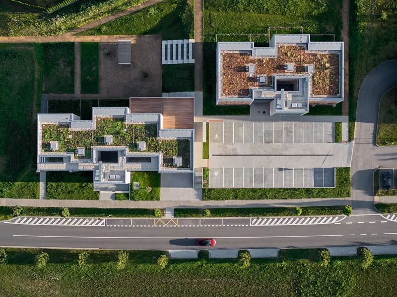 Aerial view showing vegetated rooftops, parking lot and adjacent road with a red car passing