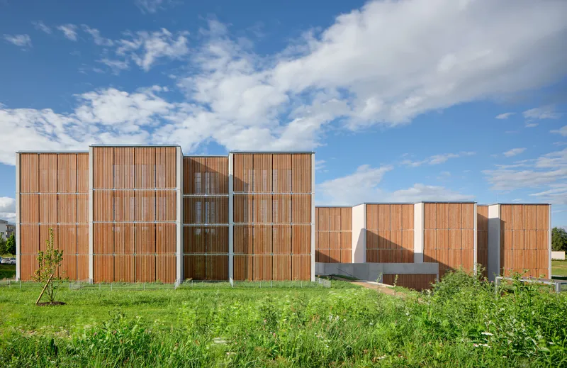 Side elevation revealing timber screening panels, white concrete volumes and an exposed exterior staircase under blue sky