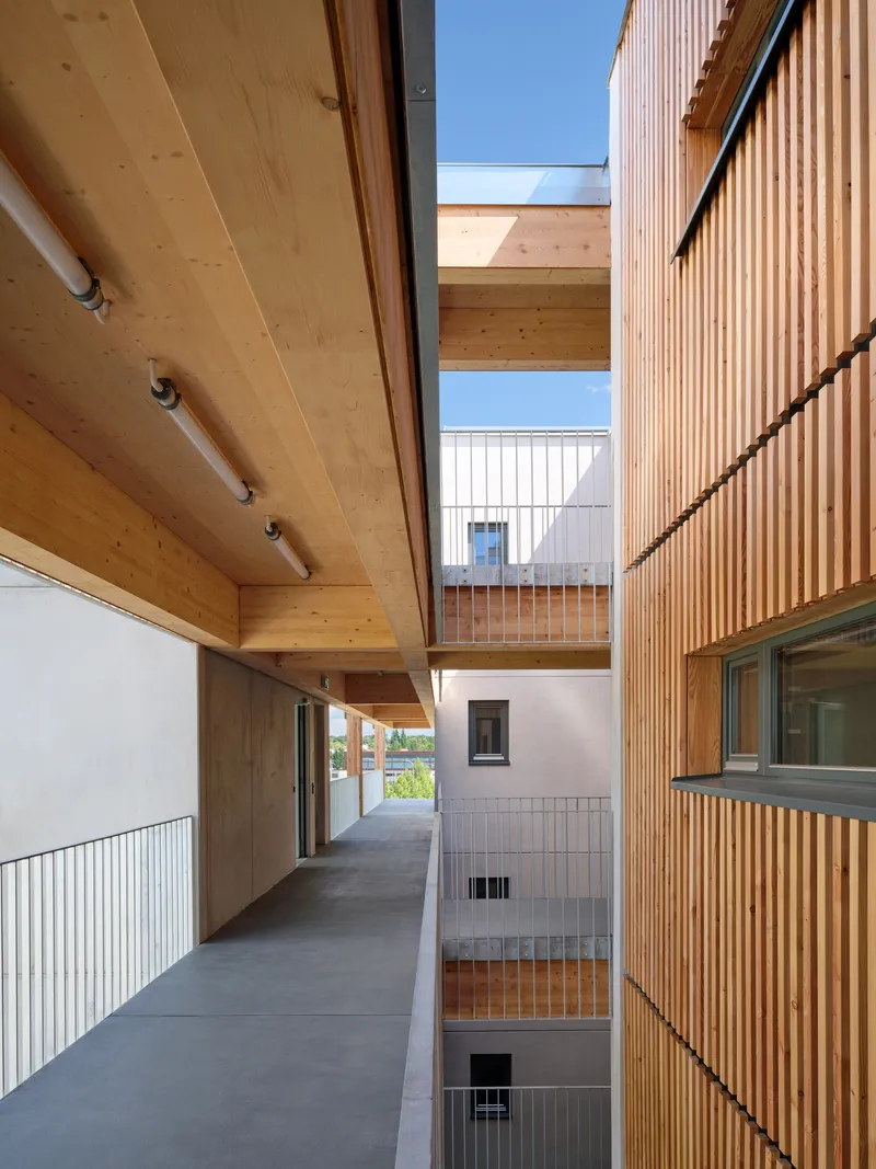 Covered upper-level walkway with timber ceiling, steel railings and view through to timber slat screens opposite