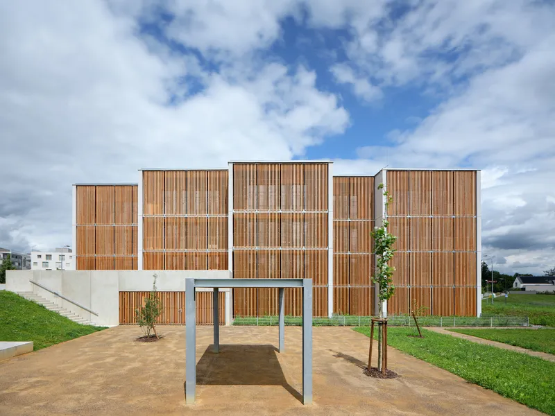 Modular timber screen facade with horizontal slats on concrete podium under partly cloudy skies