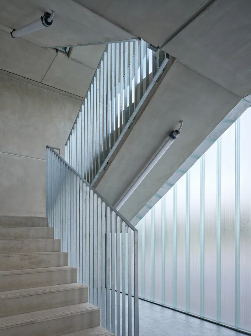 Concrete staircase with vertical metal railings and translucent wall panels filtering daylight