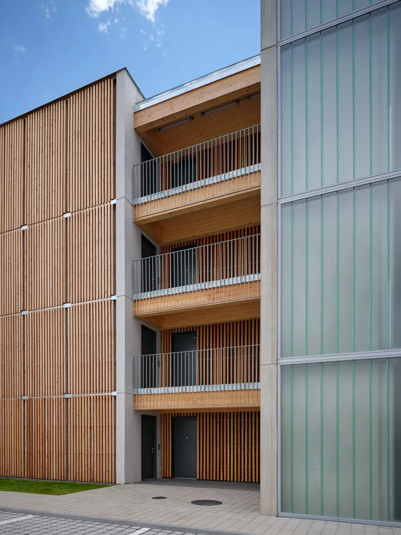 Recessed balconies with timber ceilings and metal railings between corrugated metal wall and vertical slat facade