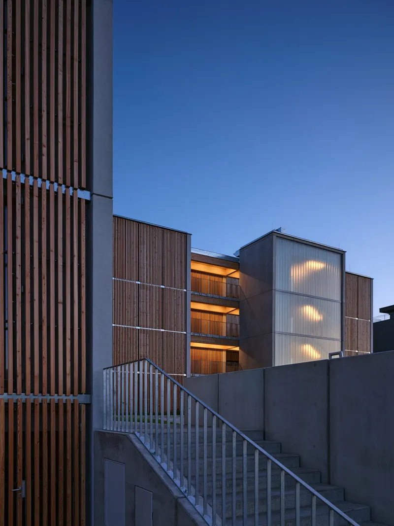 Vertical timber louvered facade and translucent stairwell with illuminated interiors at dusk