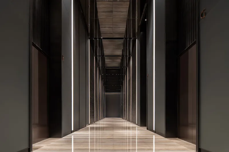 Long hallway with dark metal panels, vertical cable detailing and linear ceiling lights reflecting on polished floor