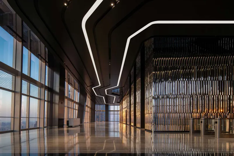 Corner lobby view showing curtain wall, decorative metal screen partition and angular ceiling light at twilight