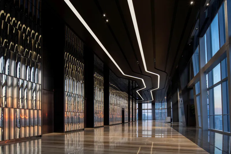 Lobby passage with metal screen wall panels, reflective floor and angular ceiling light leading to glazed entrance