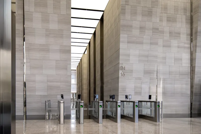 Lobby hall with stone tile walls, security turnstiles on polished floor and linear skylight overhead