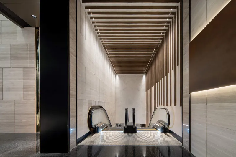 Escalator descending under a slatted timber ceiling with recessed lighting between stone walls