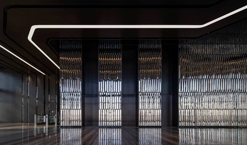 Interior lobby with backlit vertical metal screens along the far wall and linear ceiling lighting