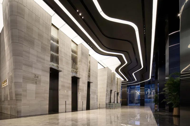 Lobby with pale stone wall panels flanked by black columns and zigzag lighting overhead