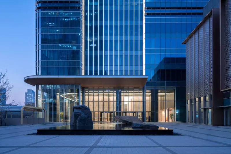 Exterior plaza with rock sculptures in a reflecting pool and glass pavilion at dusk
