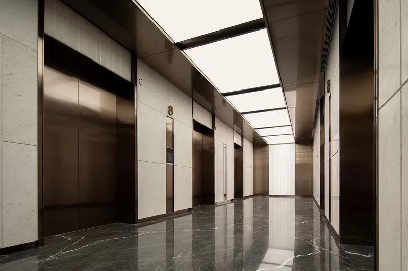 Elevator lobby with bronze-framed doors and backlit ceiling panels over dark veined marble floor