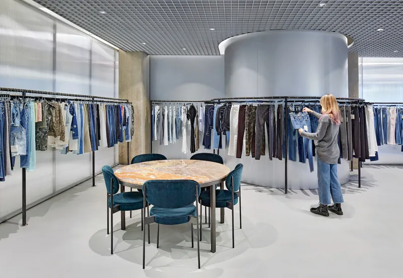 Open showroom floor with clothing racks arranged around silver cylindrical volumes and grey grid ceiling