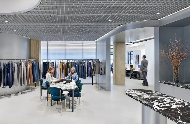View through showroom space showing clothing displays and marbled reception desk with dried branch arrangement