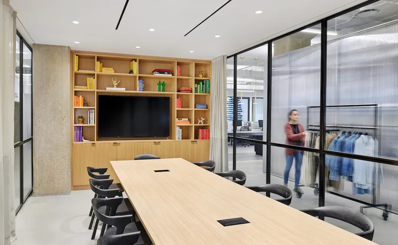 Conference room with built-in wood shelving and glass walls overlooking the clothing display area