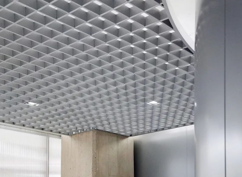 Close-up of three-dimensional grey grid ceiling system meeting concrete column and curved white soffit
