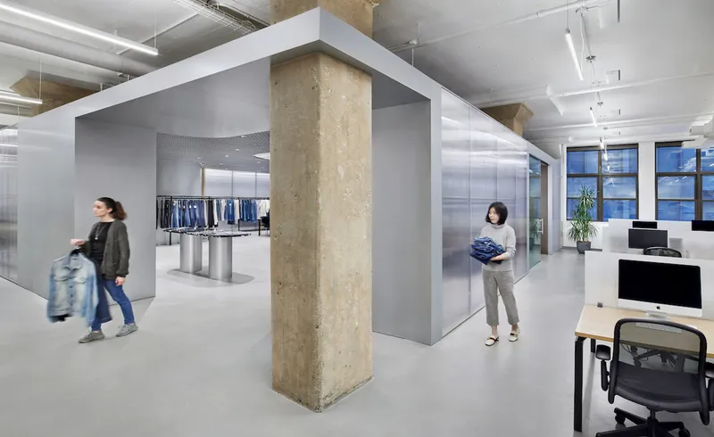 Open office floor with exposed concrete column framed by grey partitions and people in motion