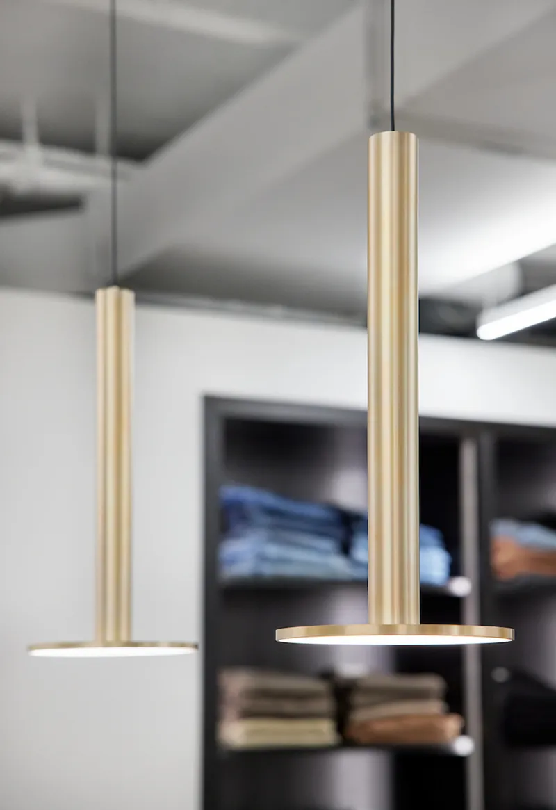 Pair of brass cylindrical pendant lights hanging above retail display shelving in background