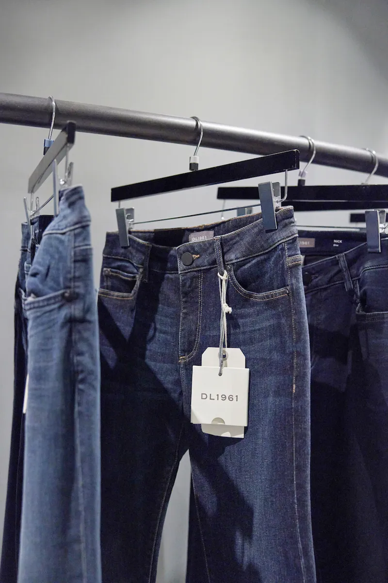 Detail of denim garments on chrome hangers suspended from exposed grey conduit pipe