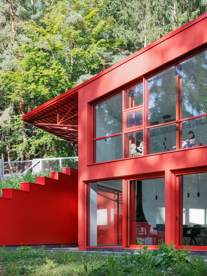 Glass doors and windows framed in red mullions with exposed triangulated roof structure above