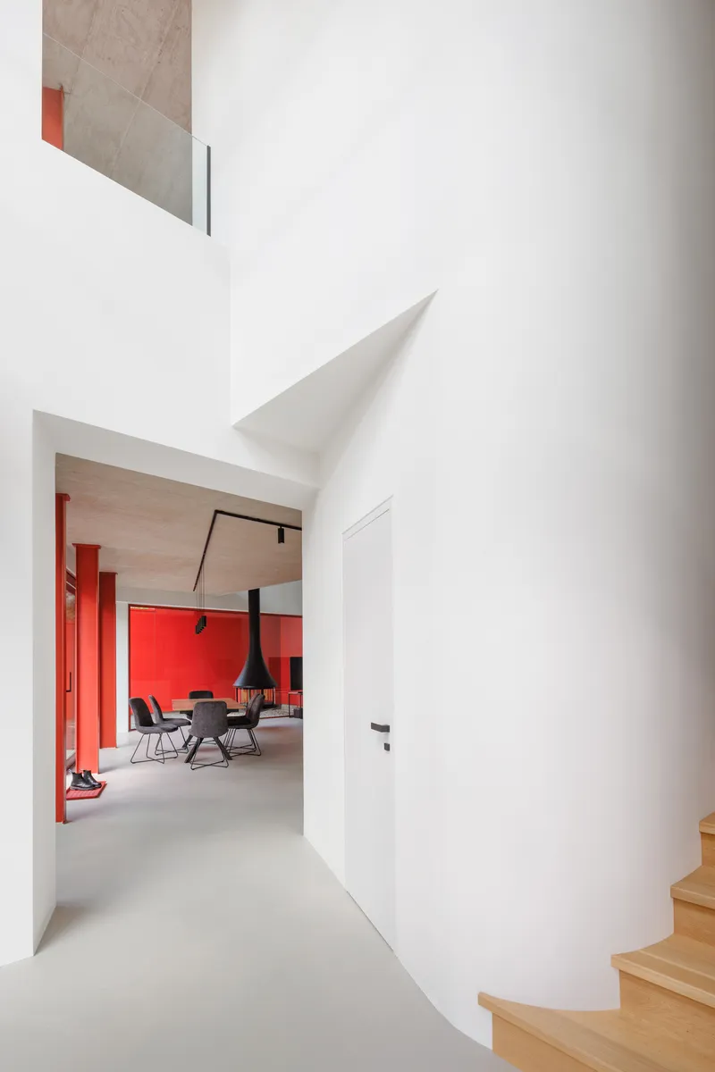 White corridor with curved cylindrical wall leading toward a room with red accent columns