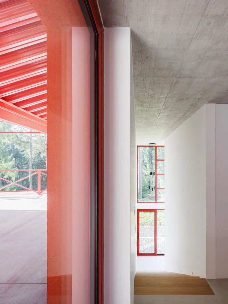 Interior threshold showing red steel door frame beside board-formed concrete ceiling and red louvered terrace beyond