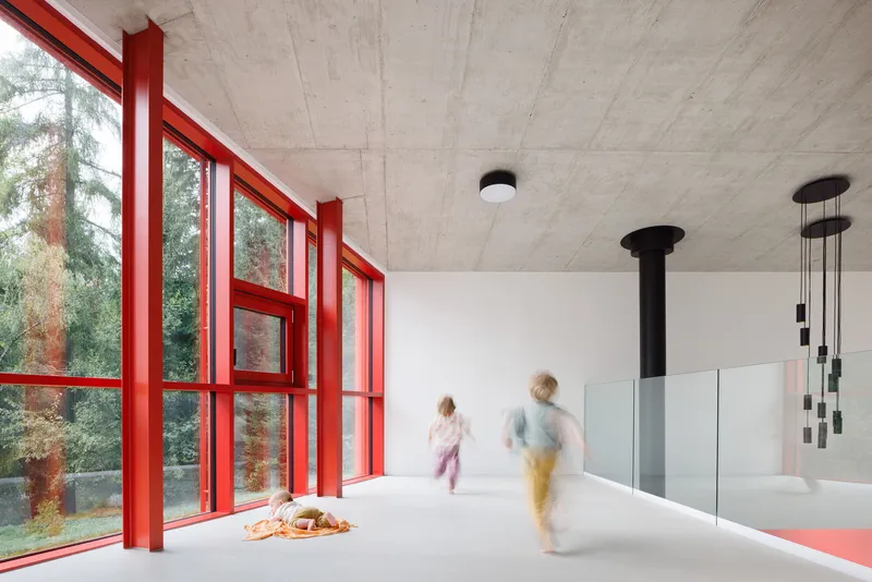Interior with red window mullions, exposed concrete ceiling, and two figures in motion blur