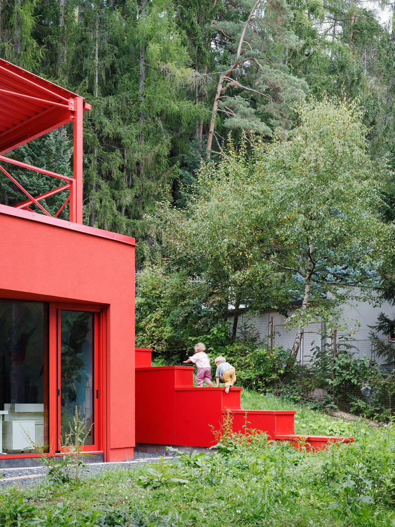Red steel staircase descending through garden with children walking beside sliding glass doors