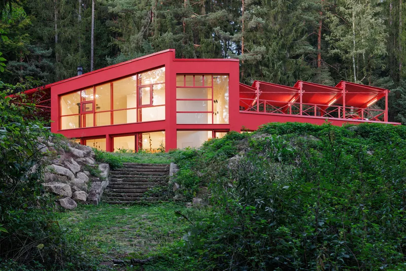 Illuminated glass facade rising above stone steps through sloping woodland at dusk