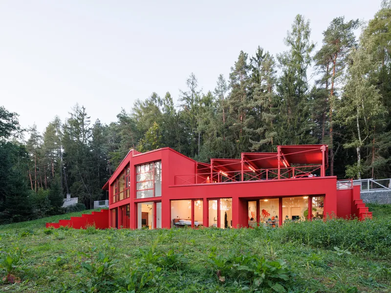 Garden elevation showing the lit interior through glazed openings in dense green vegetation