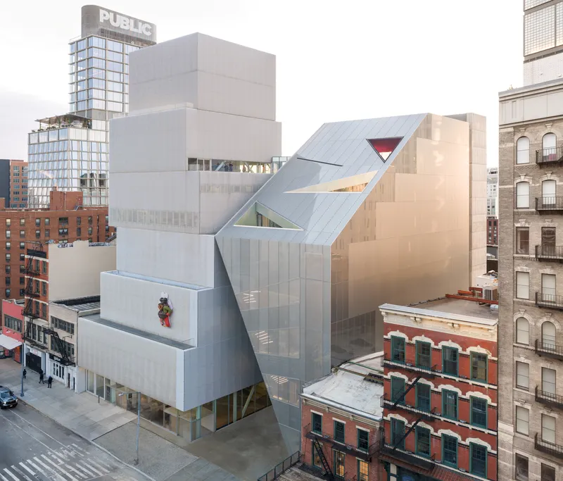 Aerial view of the stacked zinc-clad volumes rising above neighboring brick buildings in afternoon light