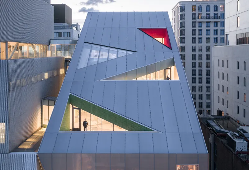 Close view of the metal-clad facade with triangular window openings illuminated at twilight