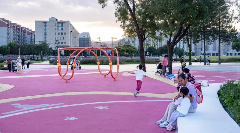 Pink play area with orange tubular sculpture and families gathered at dusk under trees