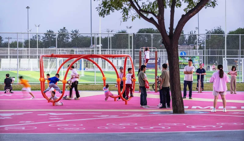 Outdoor playground with red tubular climbing frames on a pink rubber surface under an overcast sky