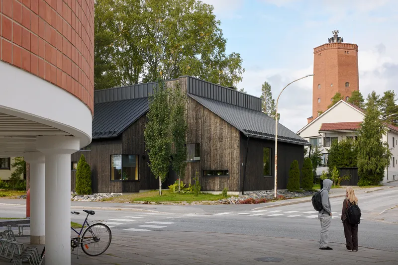 Corner lot view showing timber house with metal roof, water tower, and two pedestrians crossing
