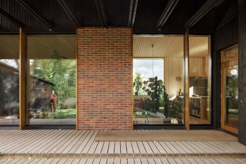 Interior courtyard with timber deck, brick fireplace wall flanked by glazed openings and person passing through garden
