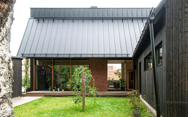 Courtyard view showing charred timber cladding, standing seam metal roof, and young tree in lawn