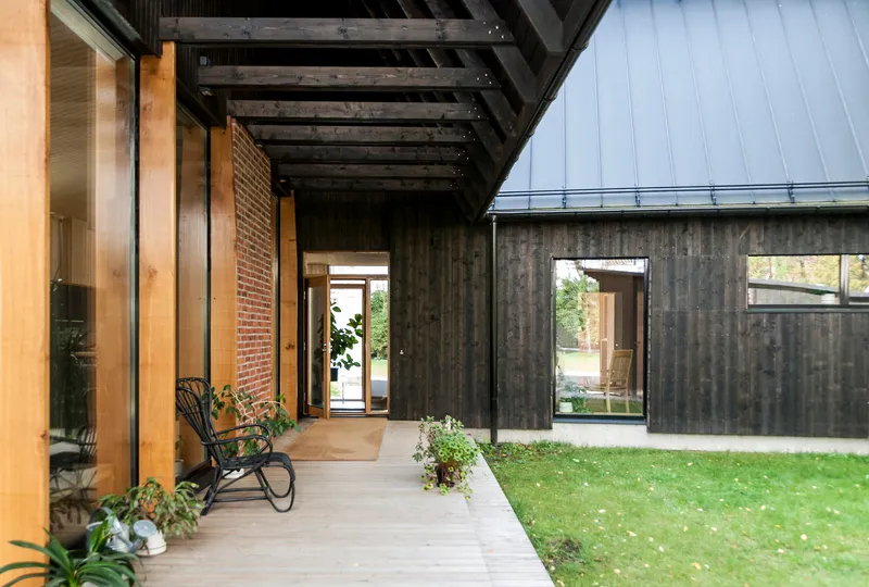 Covered walkway with exposed black-stained timber beams linking charred wood and brick volumes