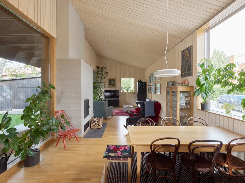 Open-plan dining and living space with light wood paneling, vaulted ceiling, and white brick fireplace